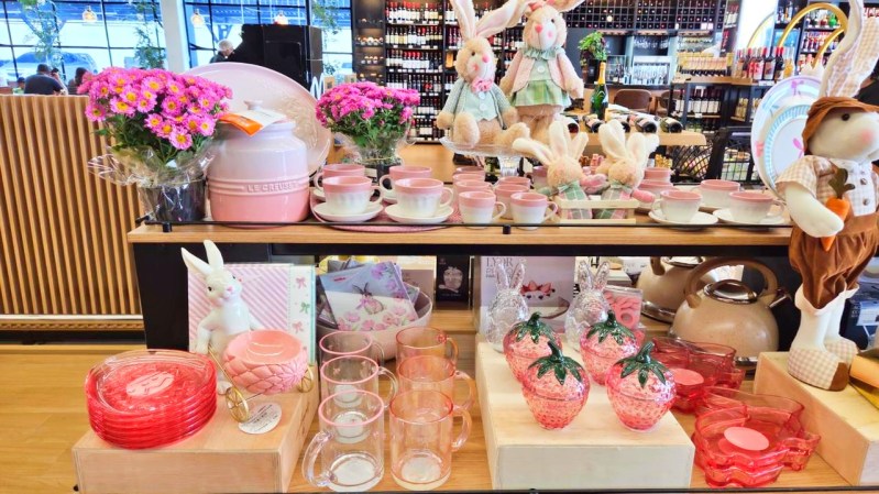 Vitrine decorada com itens de casa, incluindo coelhinhos de pelúcia, flores, utensílios de cerâmica em tons de rosa, copos de vidro e peças de decoração em formatos de frutas.