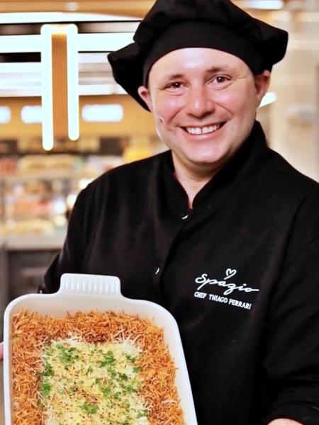 Chef Thiago Ferrari sorrindo e segurando uma travessa com um prato decorado com ervas.