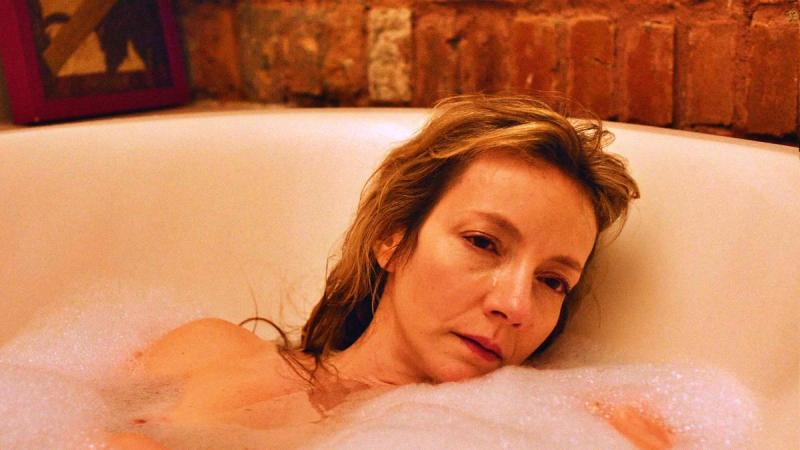 Mulher relaxando em uma banheira com espuma em um ambiente aconchegante e paredes de tijolos expostos.